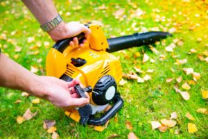 Starting-a-handheld-cordless-electric-leaf-blower-in-a-garden-selective-focus.-Autumn-fall-gardening-works-in-a-backyard